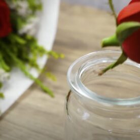 A hand putting a rose in a jar with a bunch of roses in the background.