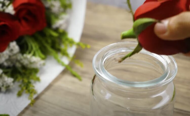 A hand putting a rose in a jar with a bunch of roses in the background.